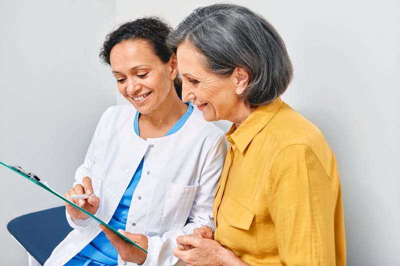 A clinician and an older woman reading through a clipboard together, both smiling